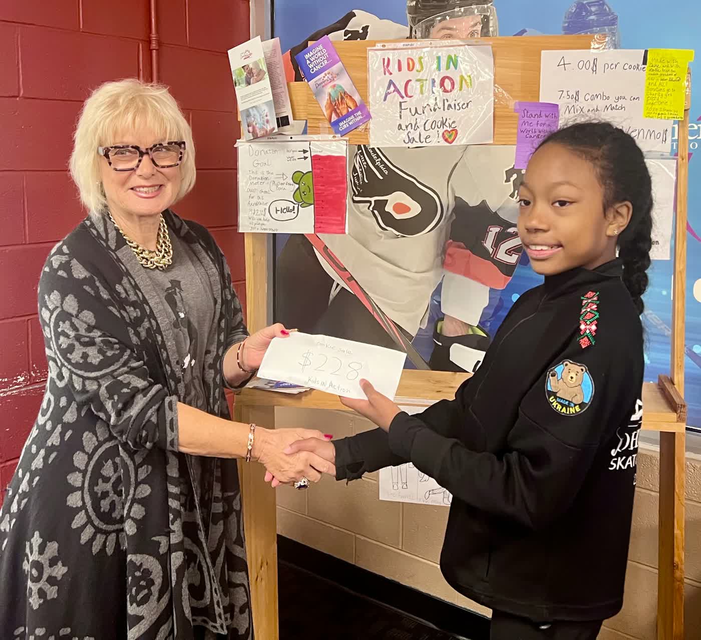 Ishara shaking hands as she donates funds raised by her Kids in Action cookie sale